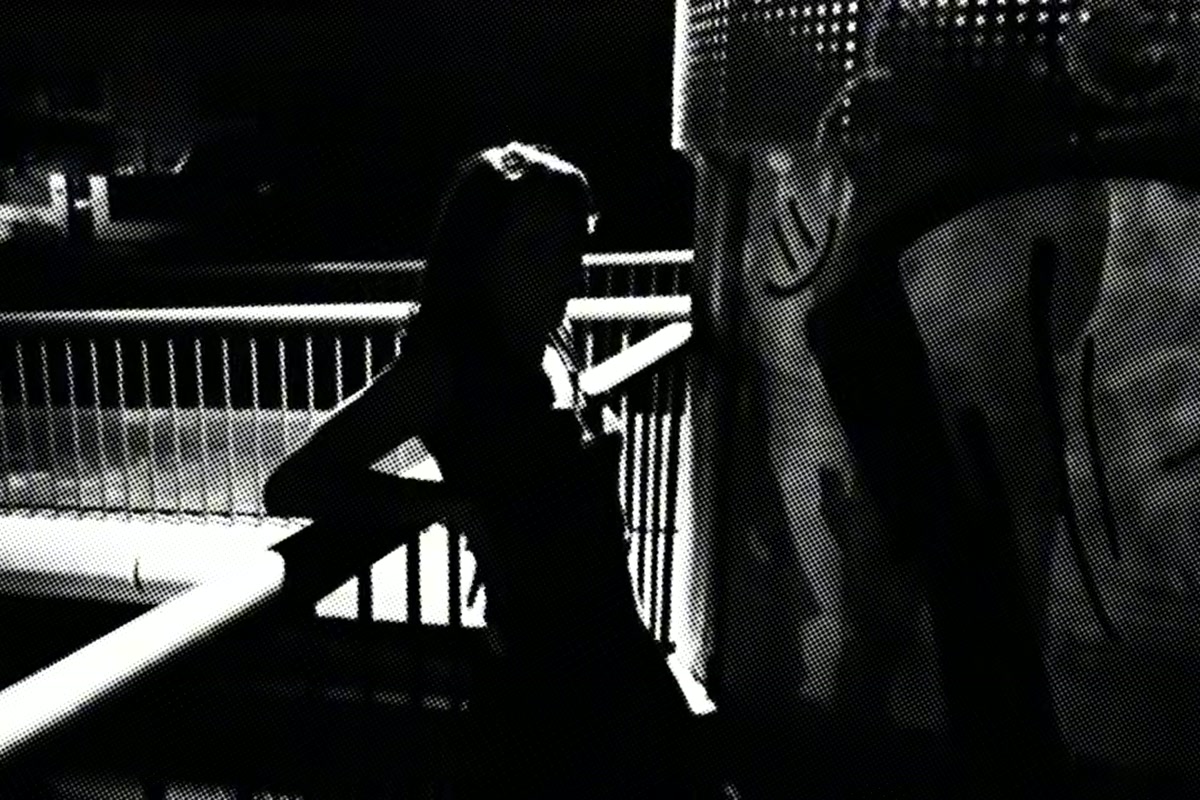 Catalina in a moody black-and-white still from her track 'waiting', seated at a railing at night, backlit.